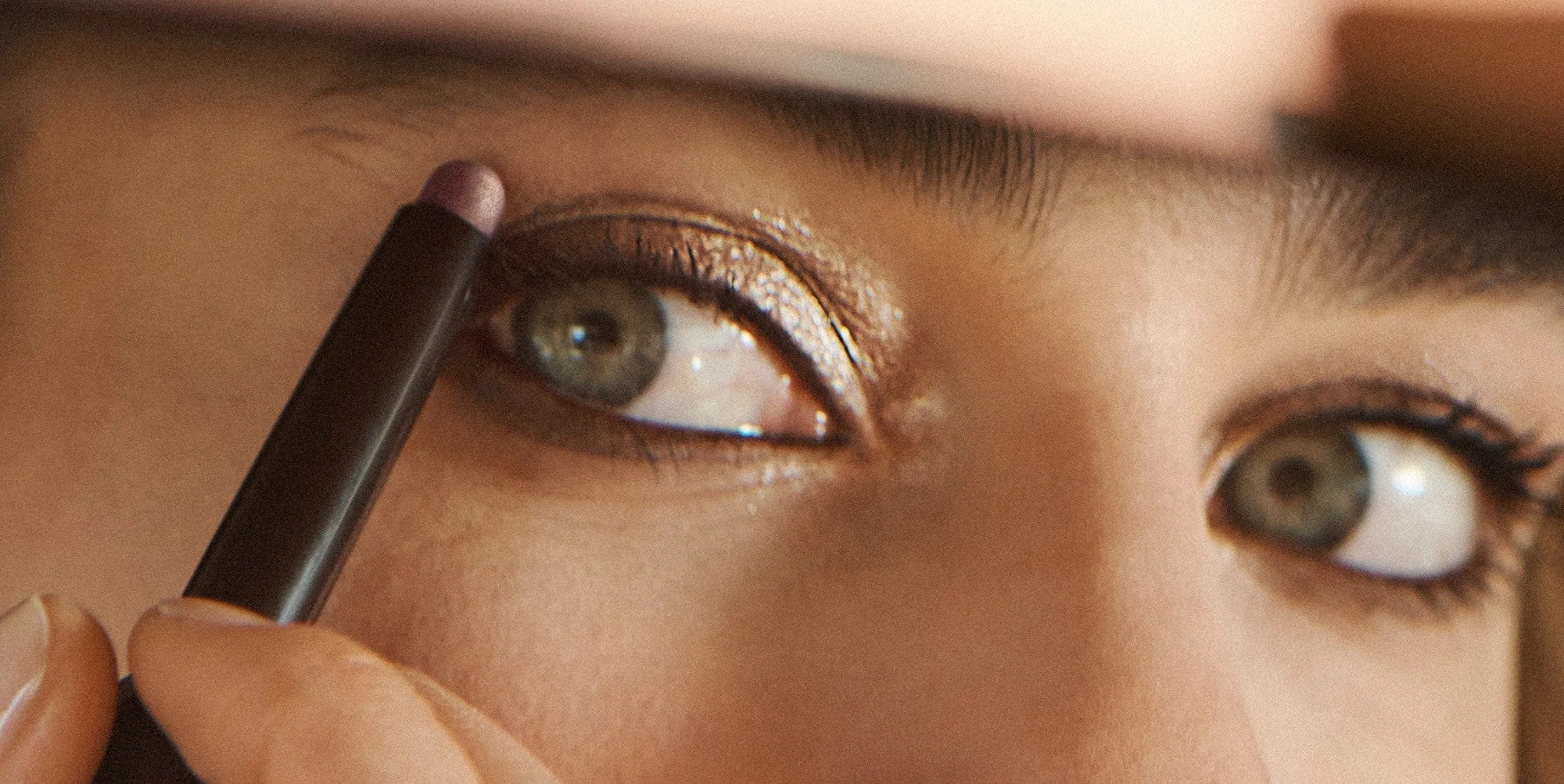 Close up of woman with green eyes applying Laura Mercier Caviar Eye Sticks on her right eyelid 