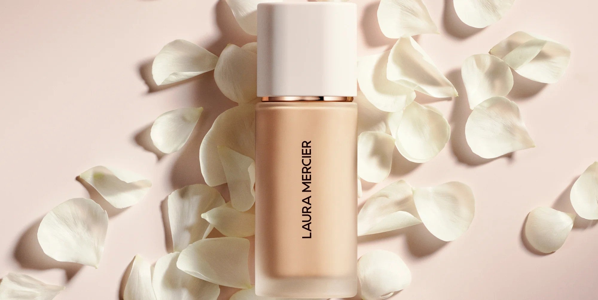 Laura Mercier Real Flawless Foundation laid down on white petals with a light pink background